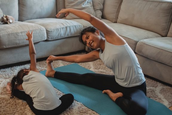 Eine Frau und ein Kind machen gemeinsam Yoga auf einer Yogamatte im Wohnzimmer.