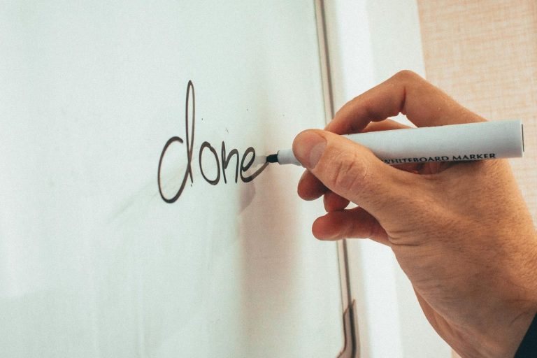 Eine Hand schreibt das Wort "done" auf eine glatte Oberfläche.