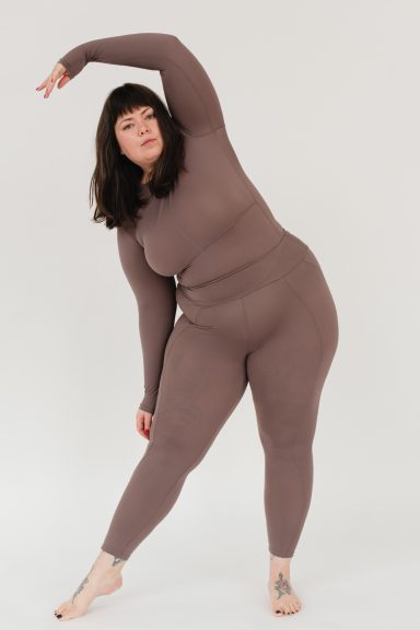 Frau in figurbetontem, braunem Outfit, die sich zur Seite dehnt.